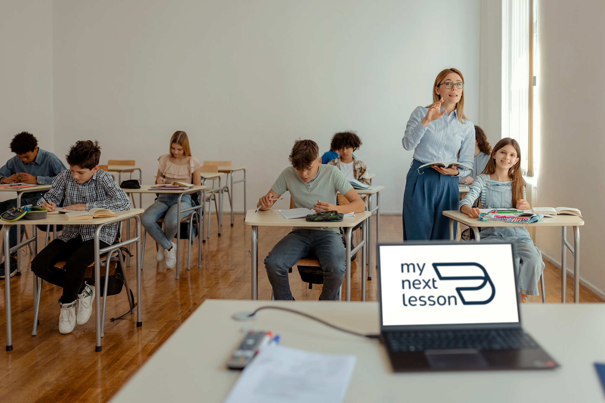 Lehrkraft mit Schulklasse im Klassenzimmer neben einem Laptop mit my next lesson Logo