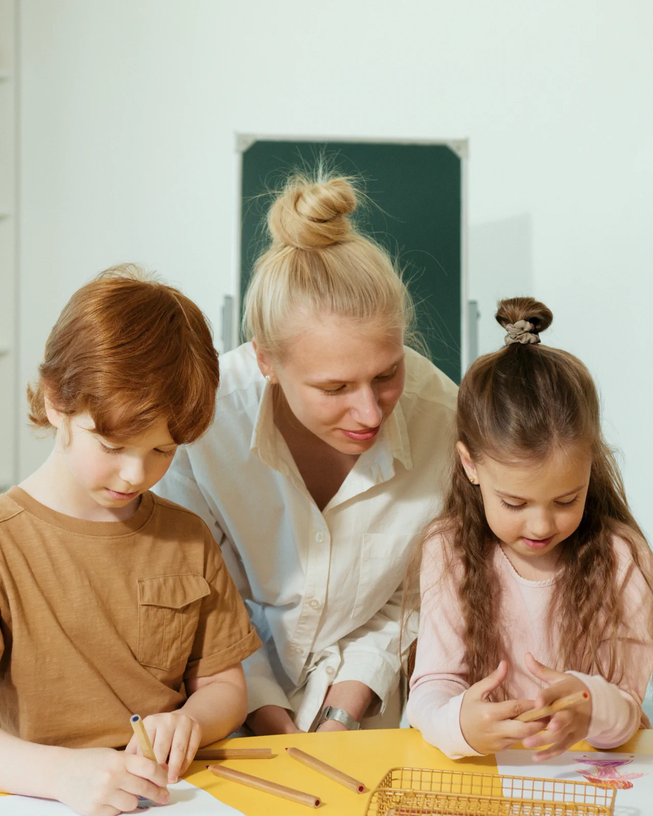Lehrerin schaut sich im Unterricht gemeinsam mit zwei Kindern die Arbeit eines Kindes an.